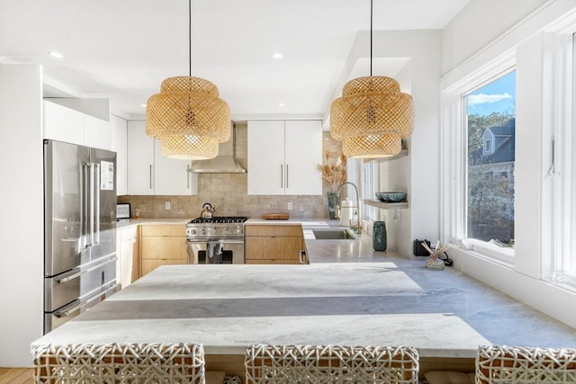 kitchen with pendant lighting, premium appliances, white cabinetry, and wall chimney exhaust hood