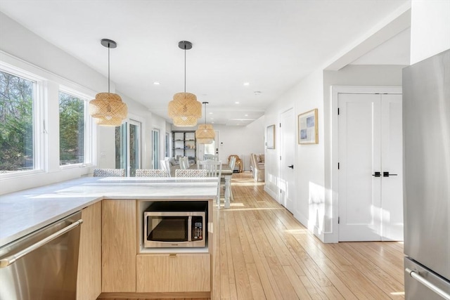 kitchen featuring light brown cabinetry, stainless steel appliances, decorative light fixtures, and light hardwood / wood-style floors