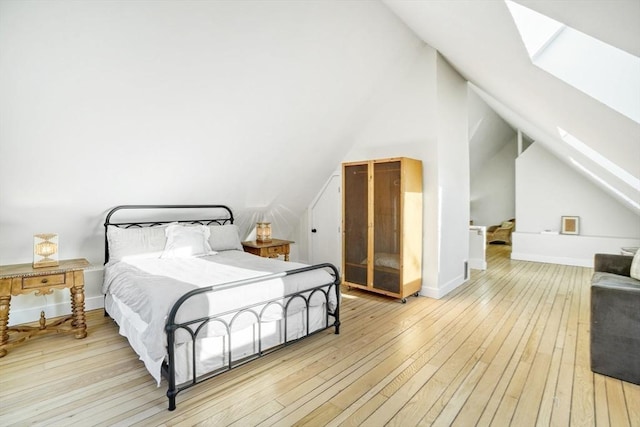 bedroom featuring lofted ceiling with skylight and light hardwood / wood-style flooring