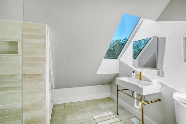 bathroom with toilet, lofted ceiling with skylight, and sink