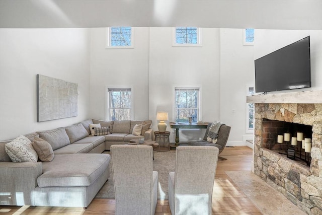 living room featuring light wood-type flooring, a fireplace, and a towering ceiling