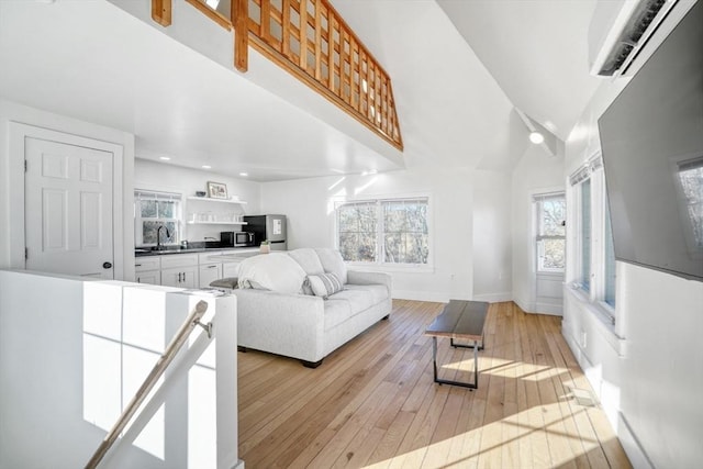 living room featuring an AC wall unit, sink, high vaulted ceiling, and light hardwood / wood-style floors