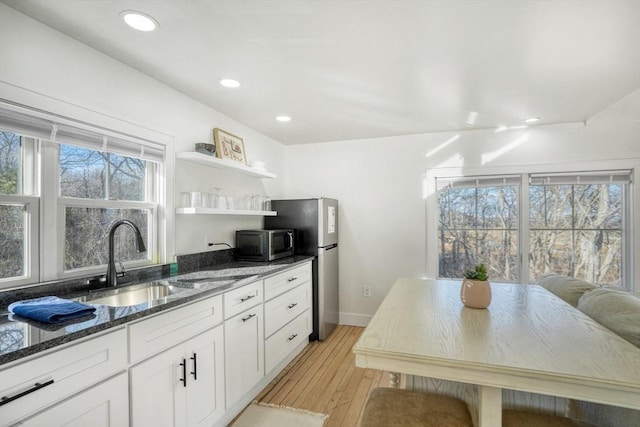 kitchen with light wood-type flooring, dark stone counters, stainless steel appliances, sink, and white cabinets