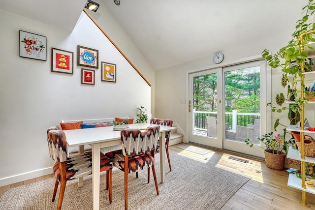 dining area with visible vents, baseboards, lofted ceiling, and light wood-type flooring