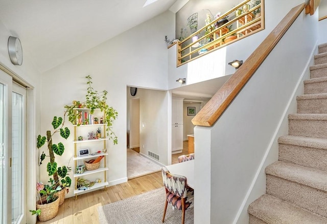 staircase with visible vents, baseboards, high vaulted ceiling, and hardwood / wood-style floors