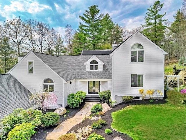 view of front facade featuring roof with shingles, a chimney, french doors, and a front yard