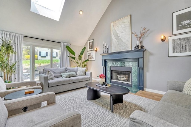 living area with high vaulted ceiling, baseboards, wood finished floors, a high end fireplace, and a skylight