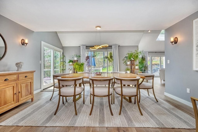 dining room with light wood-type flooring, a chandelier, vaulted ceiling, and a wealth of natural light