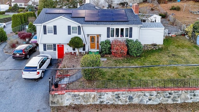 raised ranch featuring roof mounted solar panels, a chimney, a fenced front yard, and roof with shingles