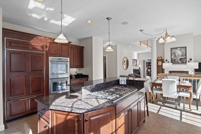 kitchen featuring a kitchen island, appliances with stainless steel finishes, dark stone counters, and decorative light fixtures