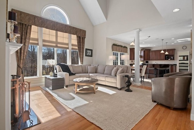 living room featuring decorative columns, high vaulted ceiling, a healthy amount of sunlight, and light hardwood / wood-style floors