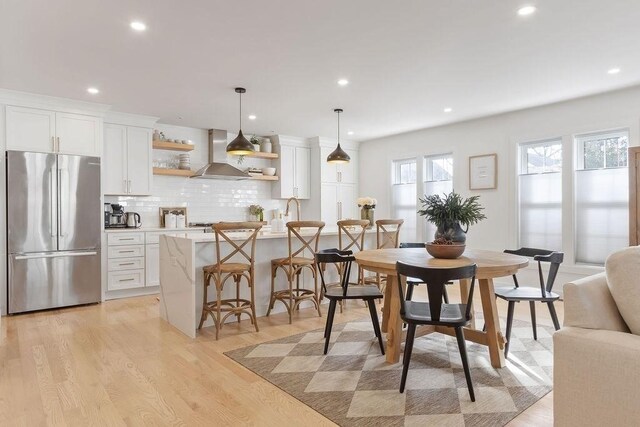 kitchen featuring stainless steel fridge, extractor fan, light hardwood / wood-style floors, white cabinetry, and hanging light fixtures