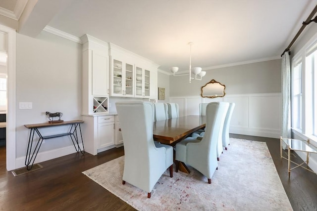 dining area with crown molding, a wainscoted wall, an inviting chandelier, and dark wood-type flooring