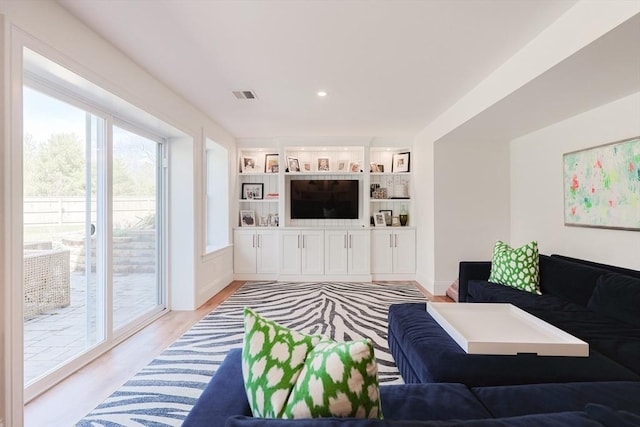 living area with visible vents, light wood-style flooring, and built in shelves