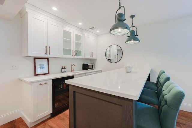 kitchen featuring visible vents, beverage cooler, light wood-type flooring, white cabinetry, and stainless steel microwave