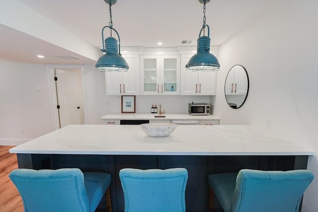 kitchen with white cabinets, a breakfast bar, light wood finished floors, stainless steel microwave, and visible vents