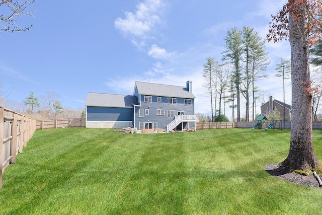 back of house featuring a fenced backyard, a playground, a yard, and a chimney