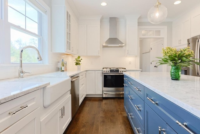 kitchen featuring a healthy amount of sunlight, wall chimney exhaust hood, a sink, appliances with stainless steel finishes, and blue cabinetry