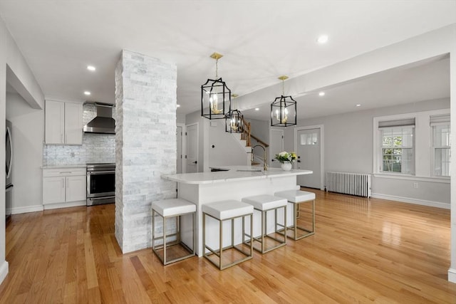kitchen with a kitchen breakfast bar, tasteful backsplash, wall chimney exhaust hood, stainless steel appliances, and light wood-style flooring