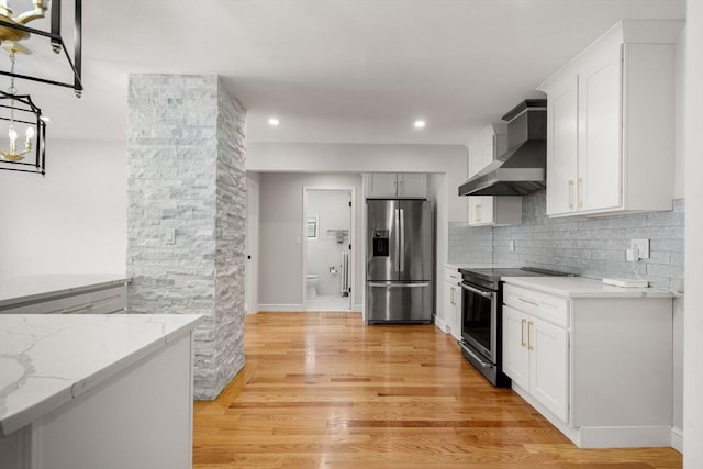 kitchen with light stone countertops, light wood finished floors, wall chimney exhaust hood, stainless steel appliances, and decorative backsplash