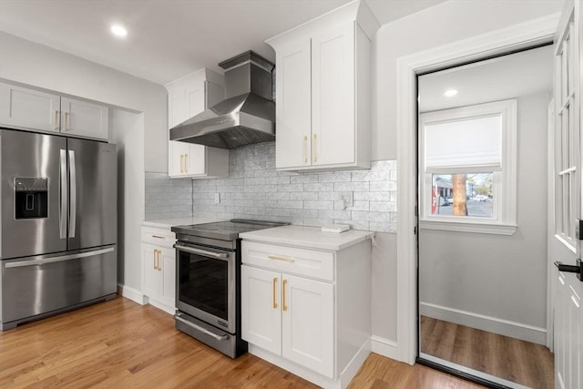 kitchen with backsplash, wall chimney exhaust hood, light countertops, stainless steel appliances, and light wood-style flooring