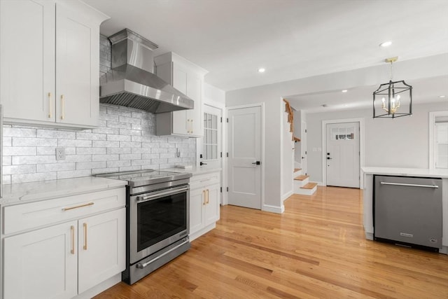 kitchen featuring wall chimney range hood, white cabinets, light wood finished floors, stainless steel appliances, and backsplash