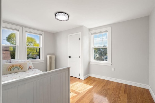 bedroom featuring baseboards, light wood-style flooring, and radiator heating unit