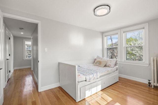 bedroom featuring baseboards, light wood finished floors, radiator heating unit, and multiple windows