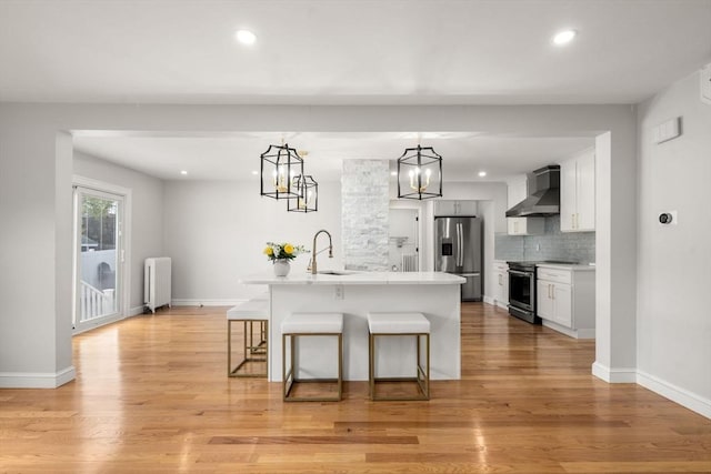 kitchen with radiator, a breakfast bar, wall chimney range hood, a sink, and appliances with stainless steel finishes