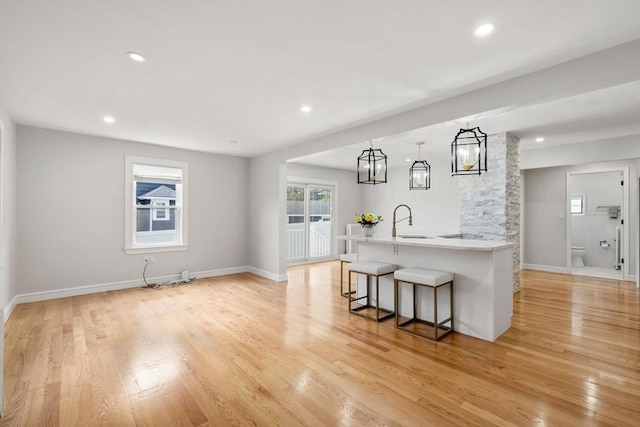 interior space with baseboards, a breakfast bar area, light countertops, a sink, and light wood-style flooring