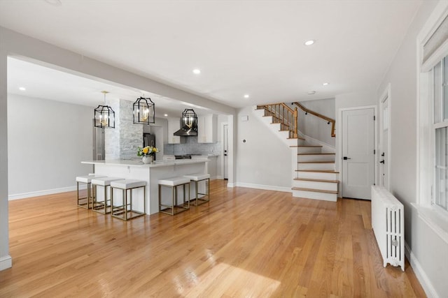 kitchen featuring a breakfast bar area, light wood-type flooring, light countertops, freestanding refrigerator, and radiator heating unit