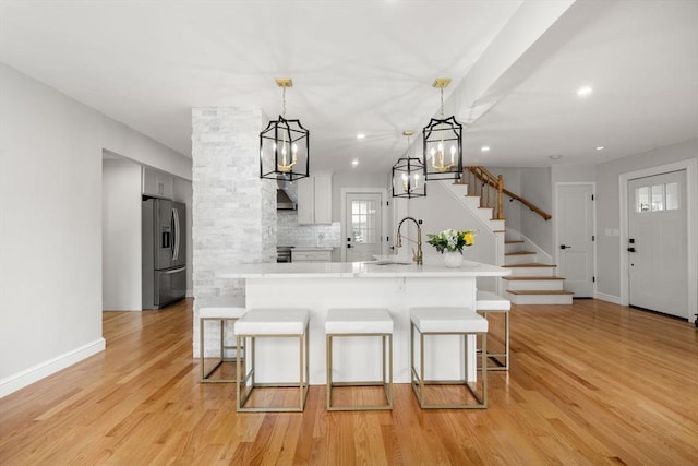 kitchen with stainless steel refrigerator with ice dispenser, a sink, a breakfast bar, and light countertops