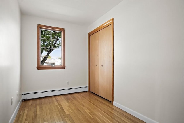 unfurnished bedroom with light wood finished floors, baseboards, a closet, and a baseboard heating unit