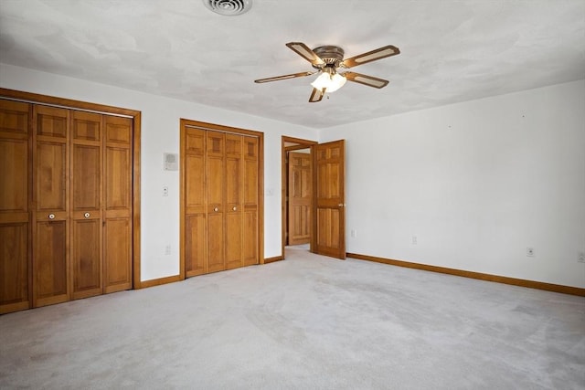 unfurnished bedroom featuring light colored carpet, two closets, visible vents, and baseboards