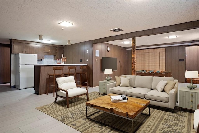 living room with light wood-type flooring, a textured ceiling, wooden walls, and visible vents