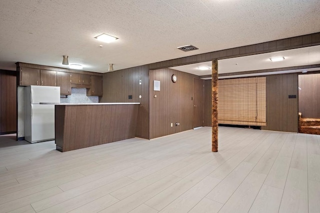 interior space with freestanding refrigerator, visible vents, wooden walls, open floor plan, and light wood-style floors