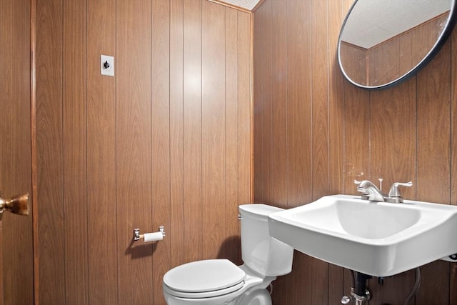 bathroom featuring a sink, toilet, and wooden walls