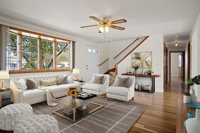 living room featuring stairs, baseboards, a ceiling fan, and wood finished floors