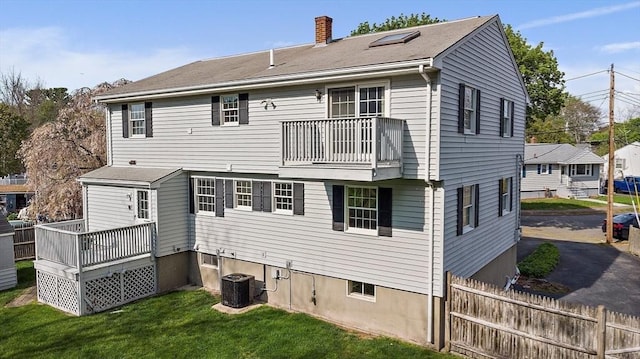back of house with fence, central AC, a balcony, a yard, and a chimney