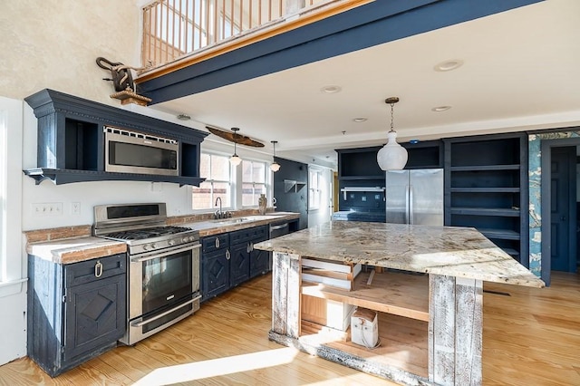 kitchen featuring open shelves, a sink, stainless steel appliances, decorative light fixtures, and light wood finished floors
