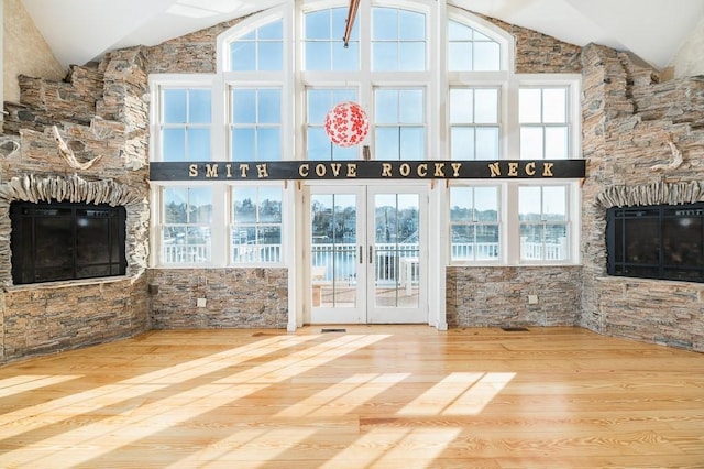unfurnished living room with french doors, wood finished floors, high vaulted ceiling, and a stone fireplace