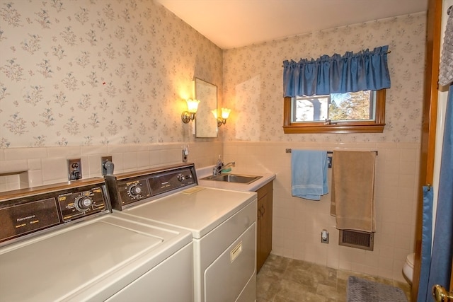 clothes washing area with washer and clothes dryer, sink, and tile walls