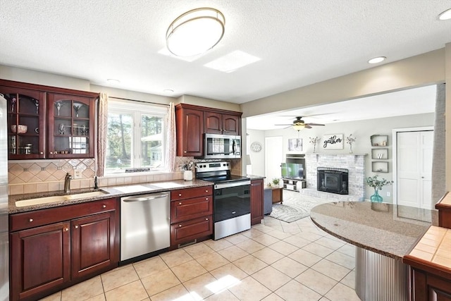 kitchen with appliances with stainless steel finishes, a glass covered fireplace, a sink, and tasteful backsplash
