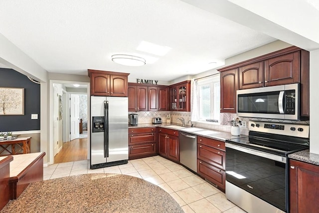 kitchen featuring glass insert cabinets, light tile patterned floors, a sink, appliances with stainless steel finishes, and backsplash