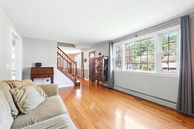 living room featuring baseboards, a textured ceiling, light wood-style flooring, and stairway