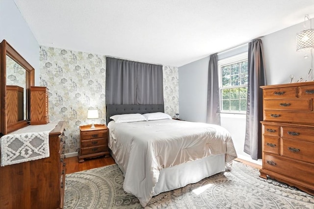 bedroom with baseboards, wood finished floors, and wallpapered walls