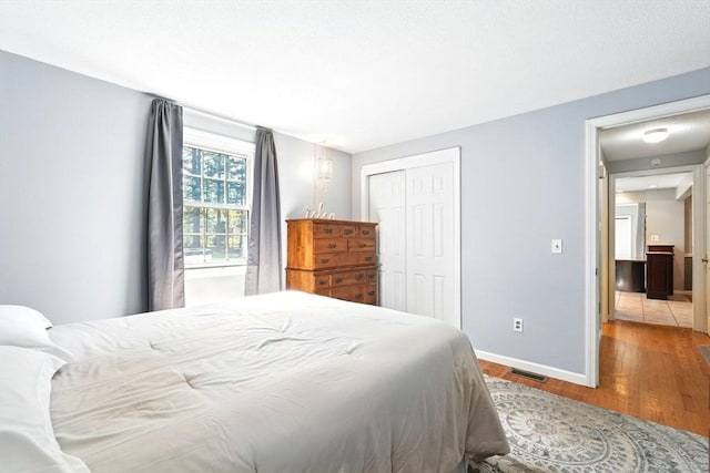 bedroom with baseboards, a closet, wood finished floors, and visible vents