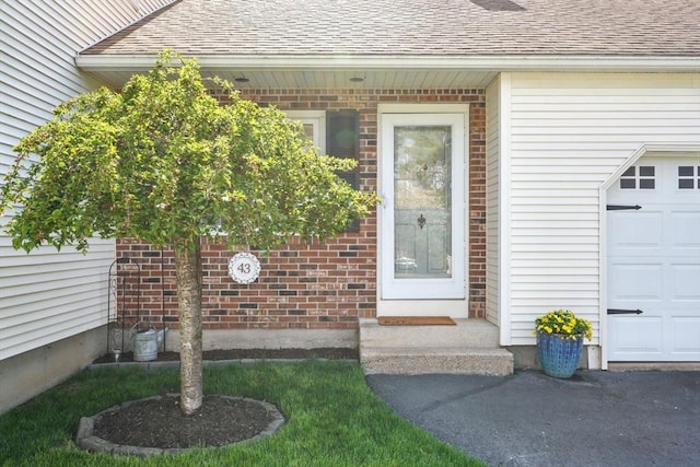 view of exterior entry featuring brick siding, a shingled roof, and a garage
