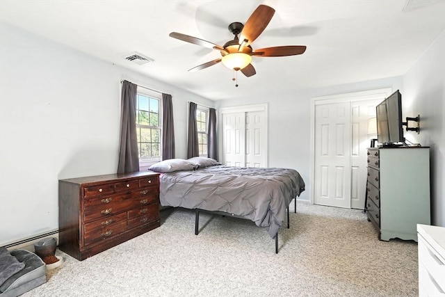 bedroom featuring a ceiling fan, light colored carpet, visible vents, a baseboard heating unit, and multiple closets