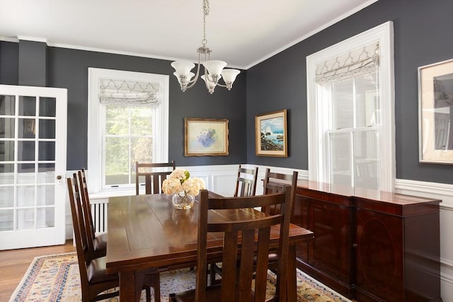 dining area featuring a chandelier, wood finished floors, wainscoting, crown molding, and a decorative wall
